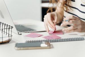 person writing on a pink sticky note